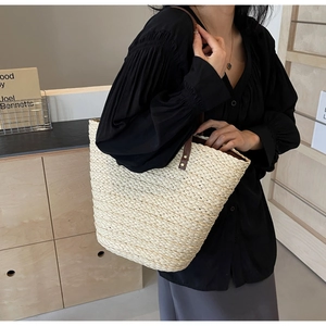 Close-up of woven straw tote bag featuring brown leather handles and rivet details