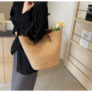 Detail of a large raffia woven tote bag with brown leather straps and tulip decoration