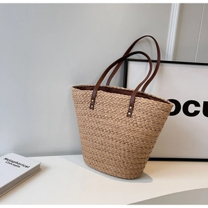 Detail view of woven straw tote bag texture with brown leather handles and metal rivets