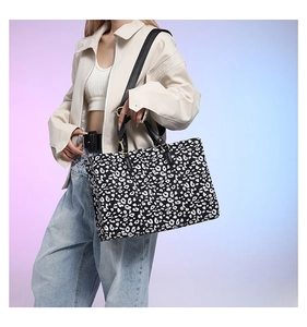 Detail of leopard print tote bag featuring black leather handles and golden hardware