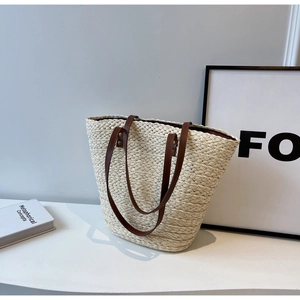 Close-up of cream woven straw tote bag with brown faux leather straps on modern display stand