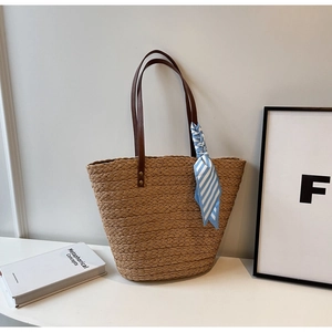 Detail of hand-woven straw tote with brown leather straps and blue striped silk scarf