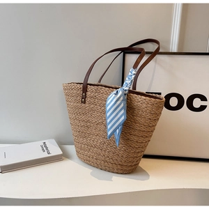 Close-up of woven straw tote bag featuring brown leather straps and striped silk scarf