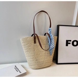Detail of raffia woven tote bag featuring leather handles and blue striped silk scarf