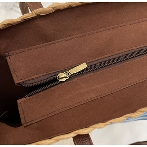 Detail view of brown canvas lining and bronze metal zipper on straw woven tote bag