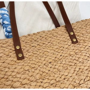 Detailed view of the straw tote bag showing raffia weaving and leather handle with rivets