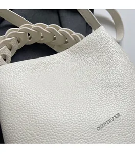 Makroaufnahme einer cremefarbenen Beuteltasche aus Leder mit Logo-Prägung