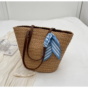 Detailed view of woven straw tote bag with brown leather straps and striped silk scarf