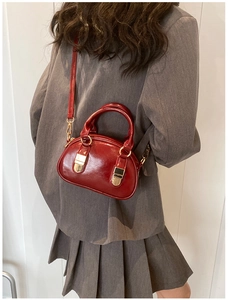 Red patent leather bowling bag worn over a grey suit to show compact size and styling