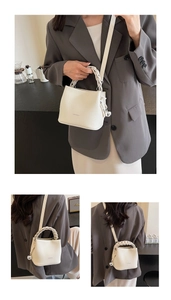 Detail der cremefarbenen Beuteltasche mit geflochtenem Griff und Silber-Charm-Anhänger