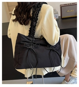 Detail of black tote bag with ruched shoulder straps and contrast stitched bow accents