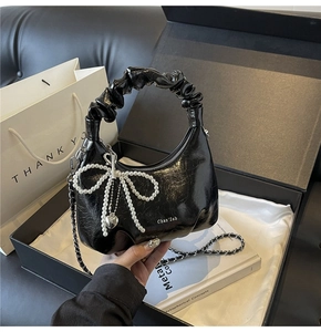 Detail of black pleated cloud bag with pearl bow charm and silver chain strap