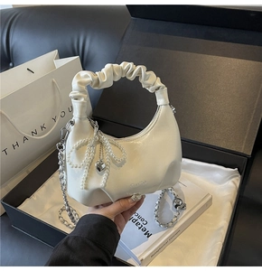 Detail view of white ruched dumpling bag with pearl bow and heart charms in a gift box