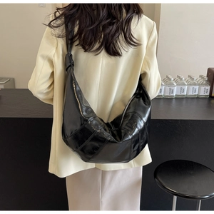 Detailed back view of model wearing a large black patent leather crescent bag with knot detail