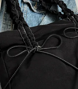 Detail of black tote bag featuring white contrast stitching and ruffled strap design