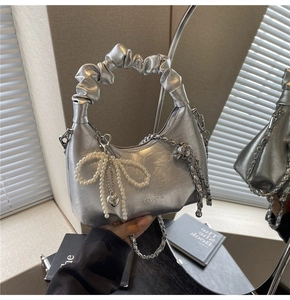 Detailed close-up of a silver cloud handbag with pearl bow charm and mirror reflection