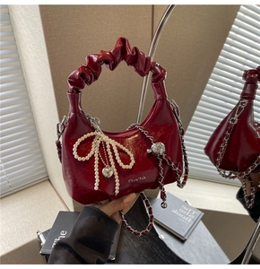 Detail of burgundy crescent bag featuring pleated handle, pearl bow, and silver heart chain