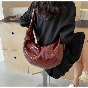 Deep red crescent hobo bag with glossy finish and knotted strap detail shown on model