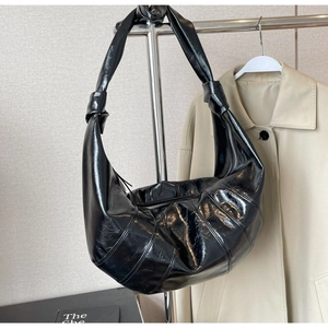 Close-up of black croissant bag with distinct stitching and decorative knotted shoulder strap