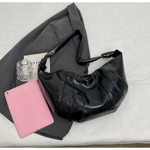 Close-up of black glossy croissant bag featuring vertical pleats and knotted strap detail