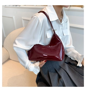 Close-up of wine red patent leather crescent shoulder bag worn by model over a silk blouse