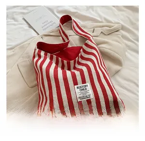 Detail view of red and white striped canvas tote bag with brand label on a bed