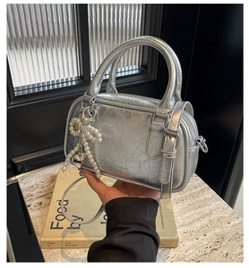 Detailed close-up of a silver metallic bowling bag featuring a pearl bow and heart charm