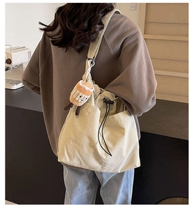 Detail of a large cream nylon tote bag with drawstring closure and cute plush charm