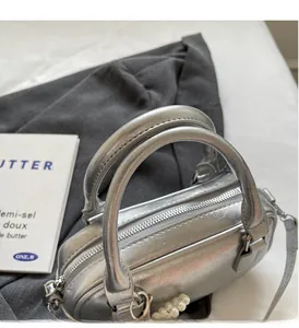 Close-up of silver Boston bag showing metallic PU texture, dual handles, and pearl charm
