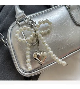 Detail of silver pleated handbag with pearl bow charm and heart-shaped metal pendant