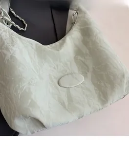Close-up of light green hobo bag with unique pleated texture and silver chain strap