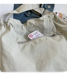 Close-up of front zipper pocket on khaki nylon tote bag showing storage capacity