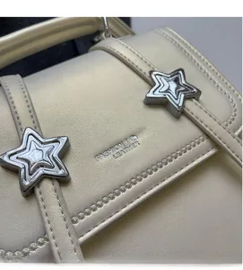 Detail der sternförmigen Metallakzente und Ledertextur auf einem beigen Rucksack