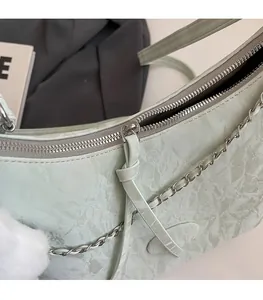Detail of mint green textured bag with silver zipper, metal chain and plush pompom charm