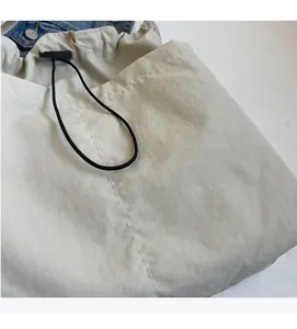 Detail of the soft off-white nylon fabric and adjustable drawstring closure on the tote bag
