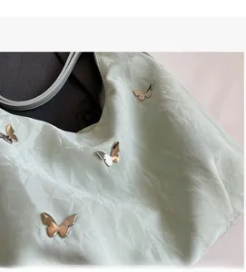 Detail of mint green tote bag featuring pleated fabric and silver metal butterflies