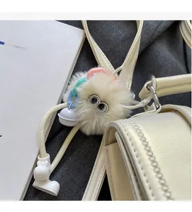 Detailansicht eines cremeweißen Plüsch-Taschenanhängers mit bunten Ketten und Glöckchen