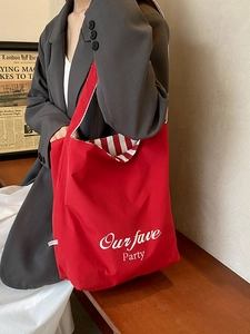 Red canvas tote bag with white lettering and striped straps in a vintage studio setting