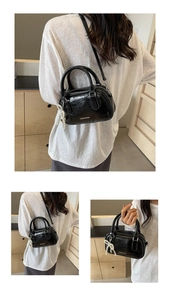 Detail of a black patent leather mini Boston bag featuring a white pearl bow charm