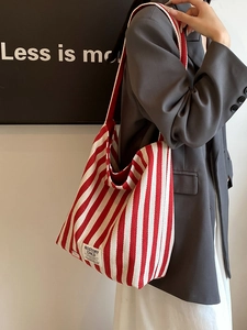 Vertical red and white striped canvas tote bag worn by a model in casual office attire