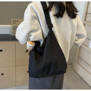 Modern black nylon hobo bag shown as a crossbody on model with coffee plush charm decoration