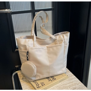 Detail einer cremefarbenen Nylon-Tote Bag mit Seitentaschen und runder Münztasche am Tisch