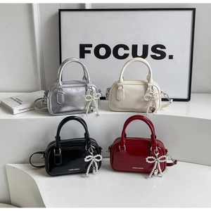 Detail view of four colorful glossy leather Boston bags with pearl bow charms on steps