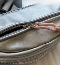 Dettaglio del tessuto metallico argento con hardware lucido e tirante della zip rosa intrecciato