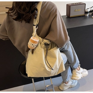 Detail of a beige nylon tote bag with drawstring closure and cute plush charm