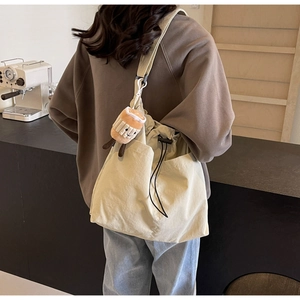Detail of cream nylon tote bag with black drawstring closure and cute plush charm pendant