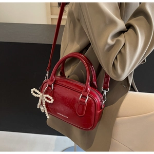 Detail of a dark red oil wax leather Boston bag with a pearl bow charm on a model
