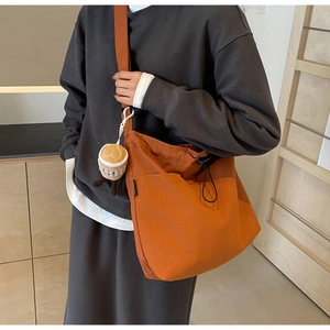 Orange nylon tote bag shown on shoulder featuring wide strap and coffee plush charm