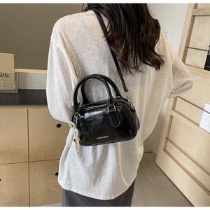 Detail of black glossy leather handbag with silver pearl tassel and branded logo