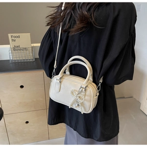 Creamy white cylinder bag with pearl bow charm and silver hardware on a model